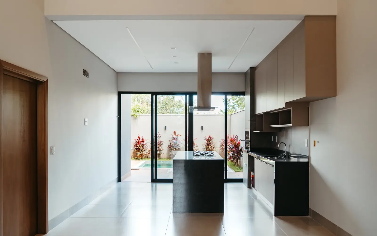 Cozinha e sala entregues, com ilha escura e porta de vidro para a área da piscina
