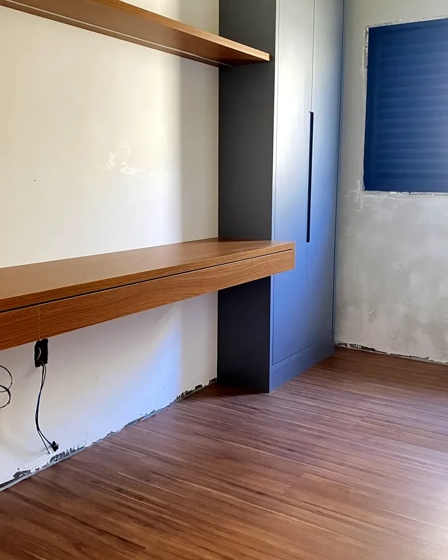 Quarto com piso amadeirado, bancada e prateleira em madeira e armário escuro