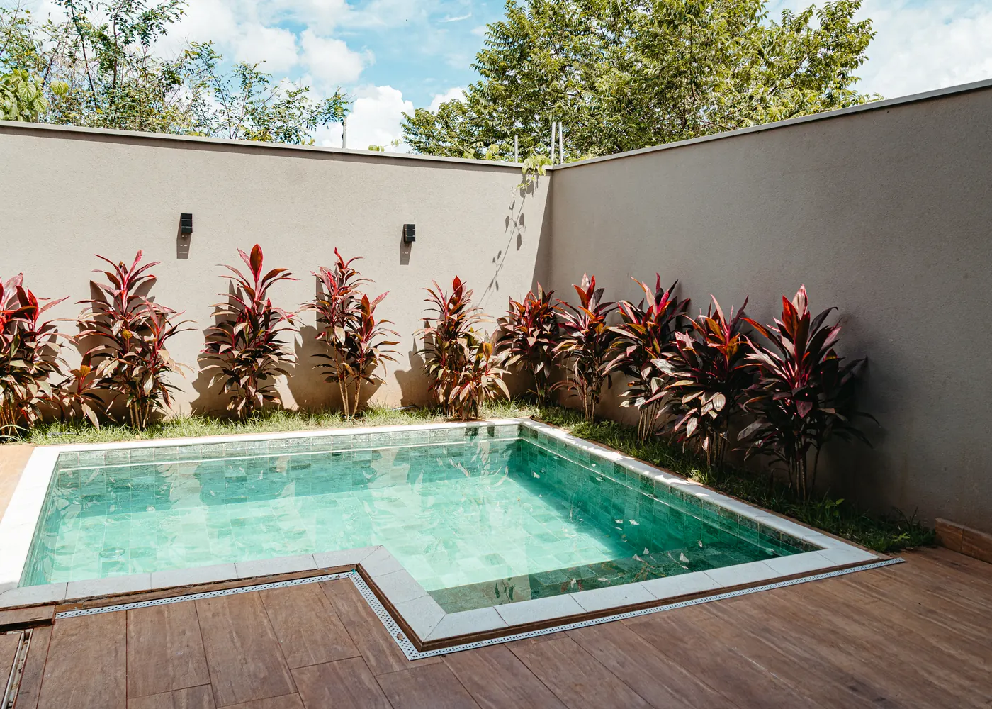 Piscina com deck de madeira e jardim de plantas vermelhas
