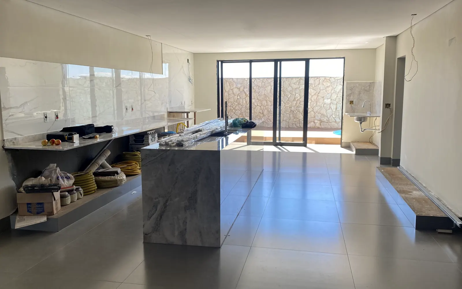 Cozinha em acabamento com ilha revestida em pedra e porcelanato de grande formato