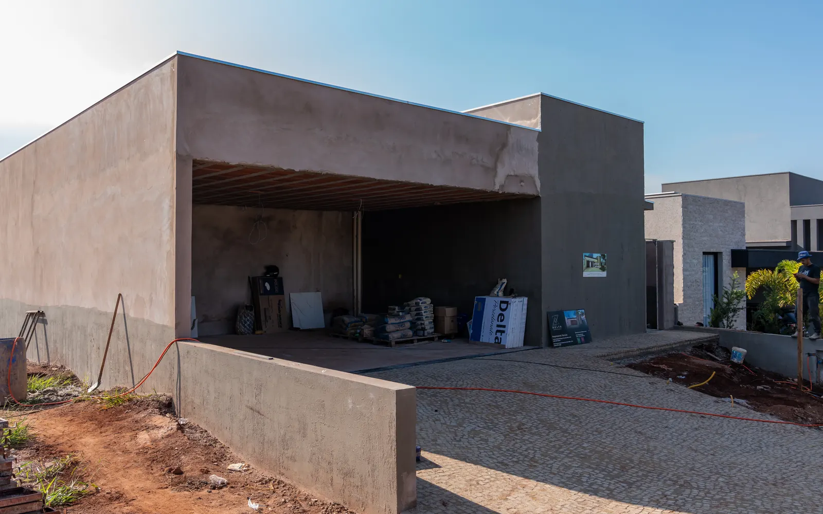 Casa em fase de obra bruta, com estrutura e reboco prontos e materiais na garagem